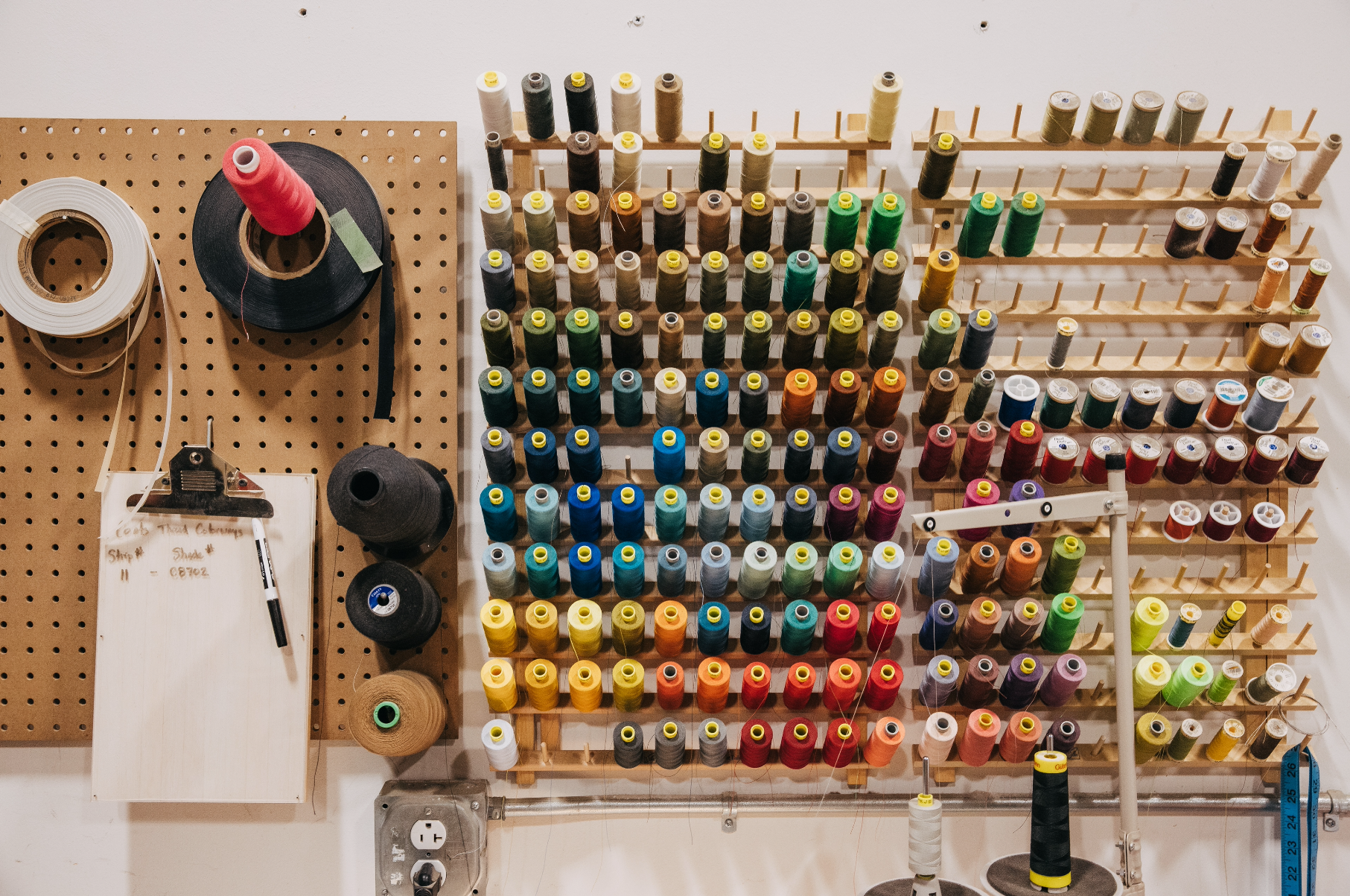 Spools of thread arranged on a wooden rack with a pegboard in the background.