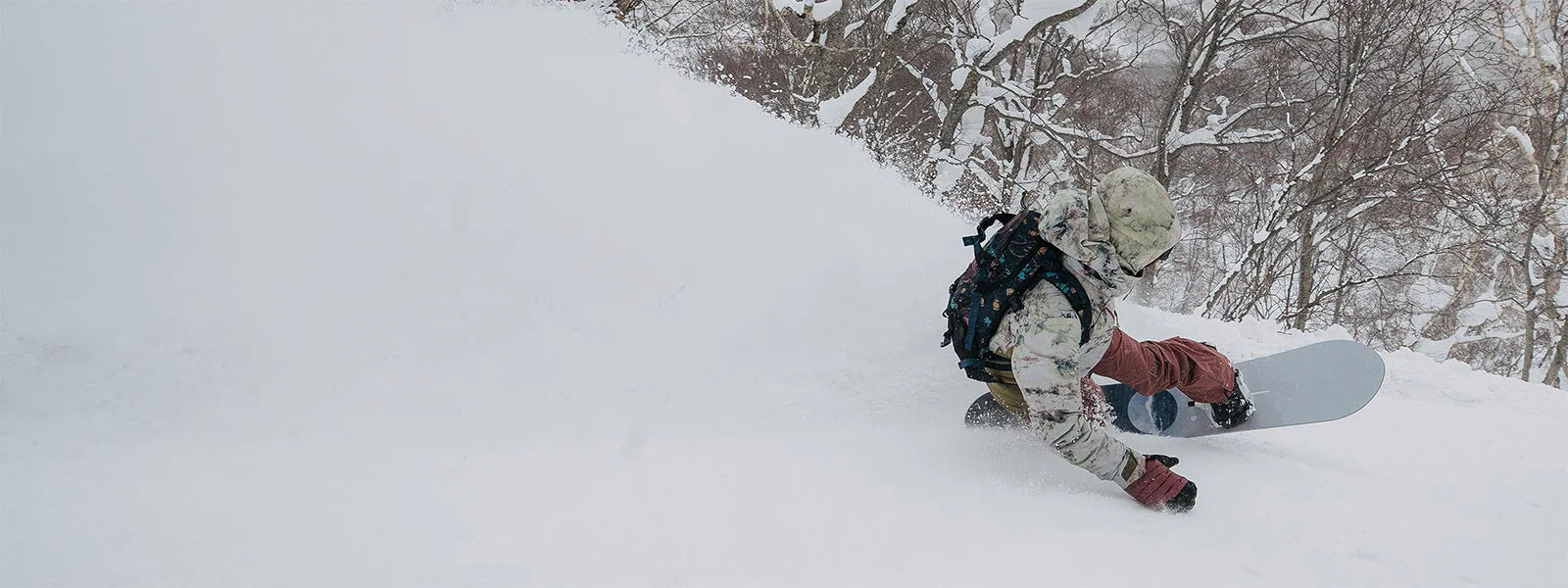 Person snowboarding down a snowy slope with trees in the background