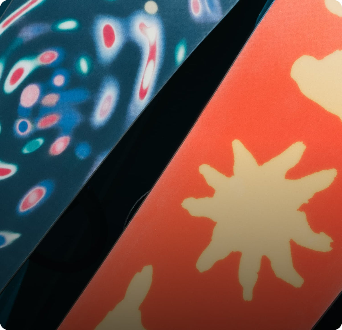 Close-up of two patterned boards or panels, one dark blue with abstract multicolor spots and one coral orange with pale cream star-like shapes, separated by a dark strip.