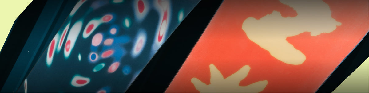 A close-up of a glossy dark surface with abstract printed or reflected patterns, including blue, pink, white, and red shapes on one side and a warm orange-red area with pale yellow abstract forms on the other.