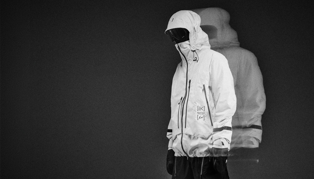 A rider stands wearing Burton AK’s white shell jacket with goggles and hood up