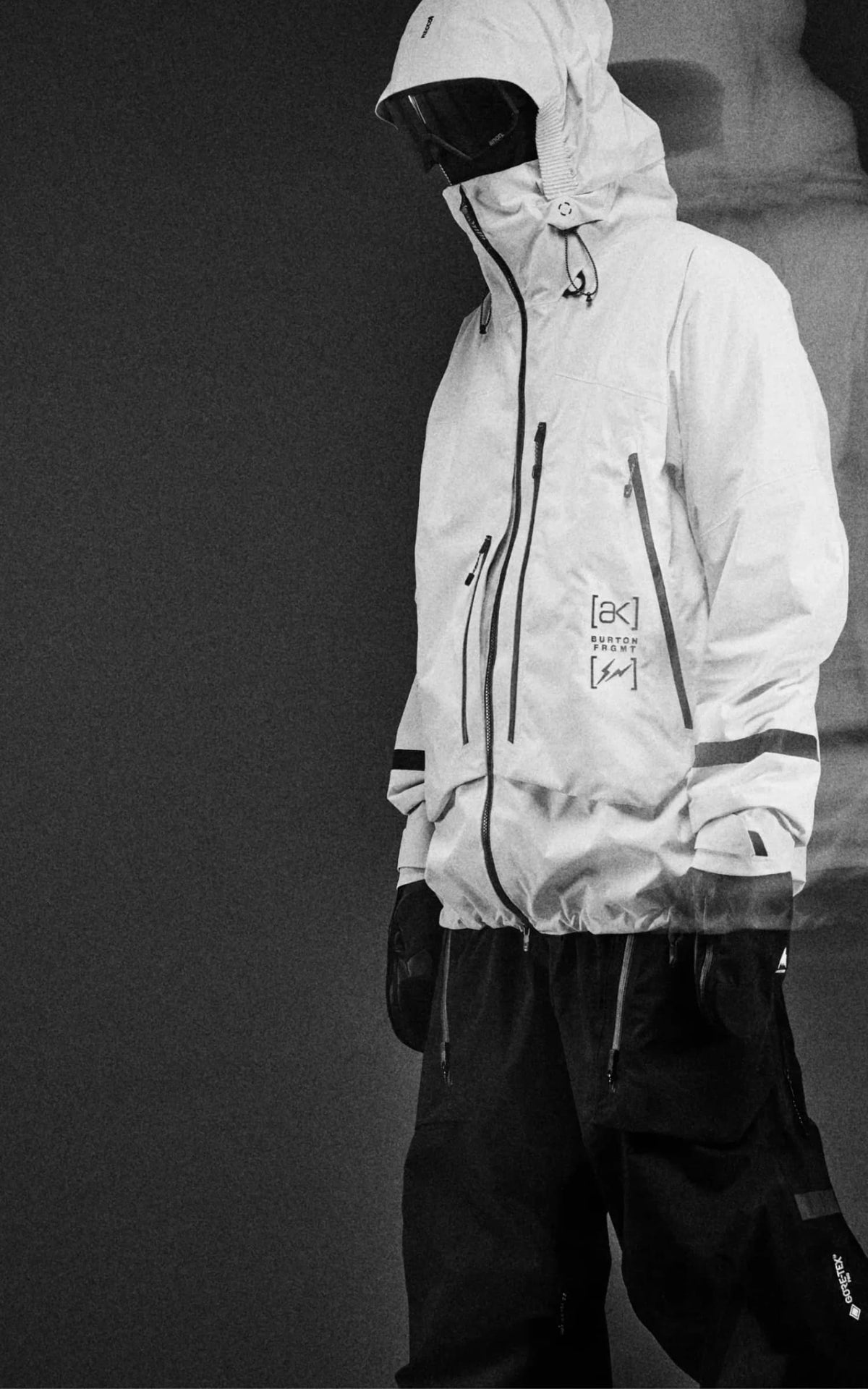 A rider stands wearing Burton AK’s white shell jacket with goggles and hood up