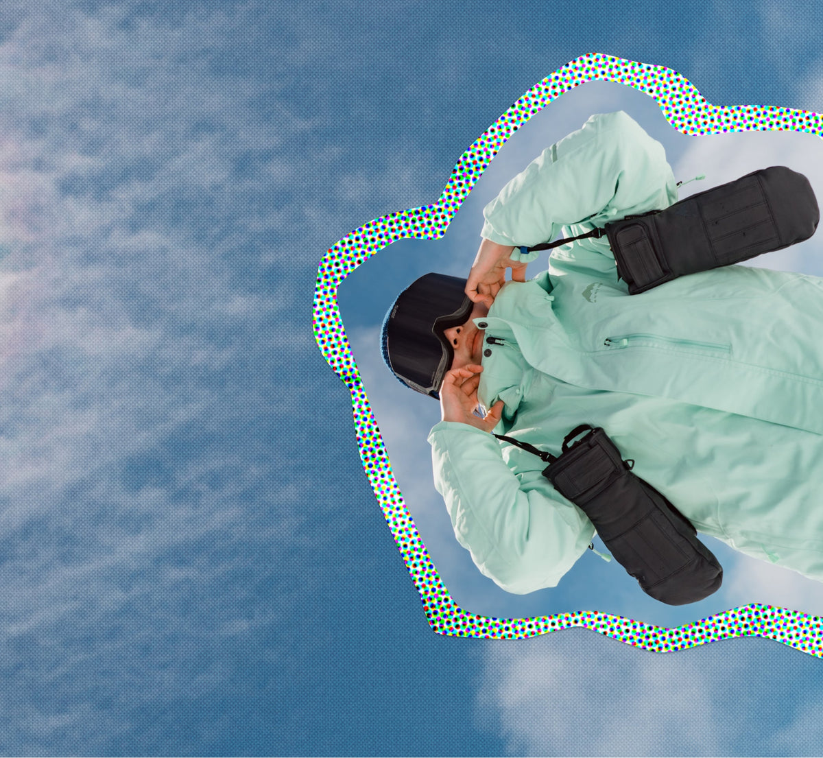 snowboarder holding gloves in front of a cloudy, blue sky