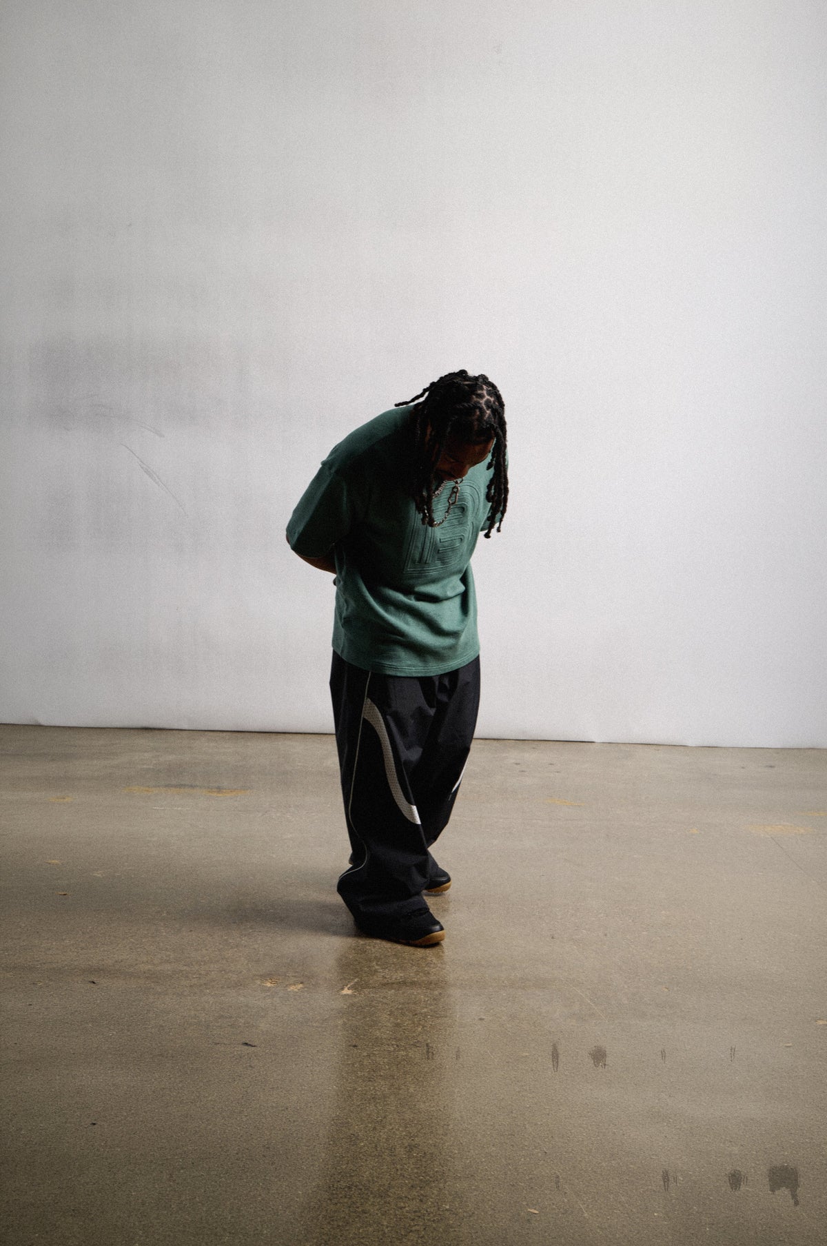 rider zeb modeling a green, embossed burton tee pared with jeans. head down in front of a white wall