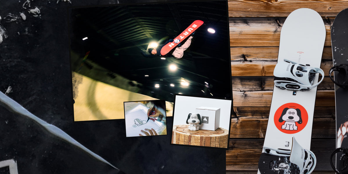 A styled flat-lay featuring a white snowboard with black bindings and a red circular logo sticker, alongside a black snowboard, a dark textured surface, and a wooden plank background with small printed photos.