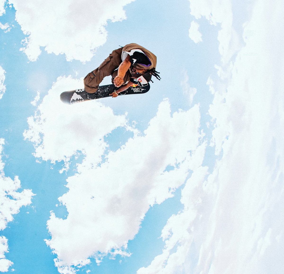 A snowboarder in mid-air performing a trick against a bright blue sky with clouds, next to large promotional text reading 'EVERY1'S INVITED'.