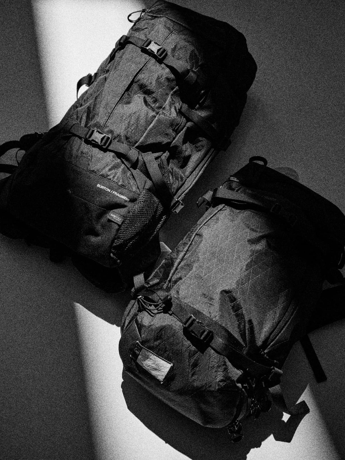 Two backpacks photographed on a gray surface with dramatic diagonal light and shadow.