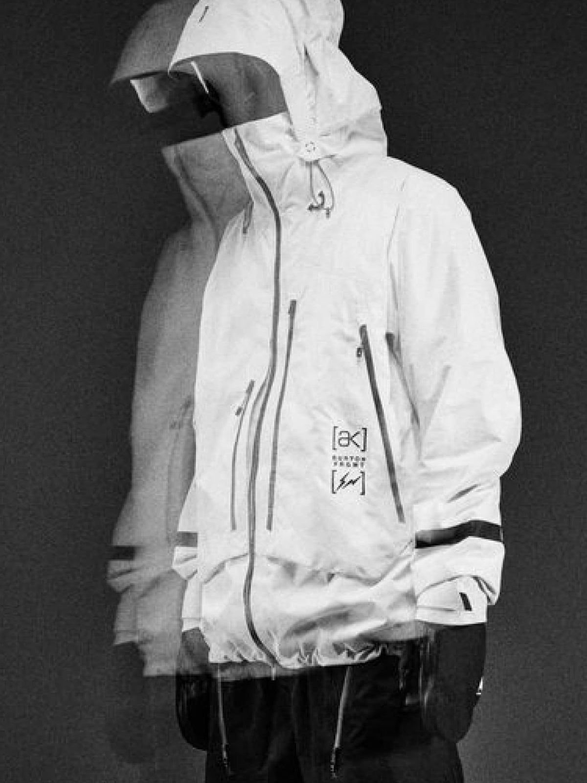 A person wearing a snowboard jacket with multiple zippered pockets and a small printed logo on the chest, shown against a dark studio background.