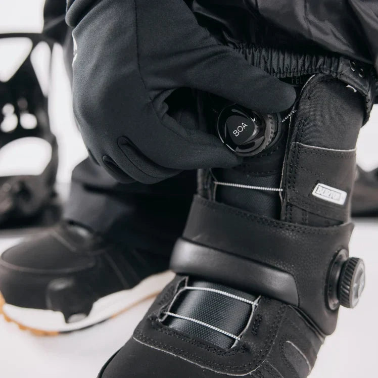 Person adjusting BOA system on a black snowboard boot with a white background