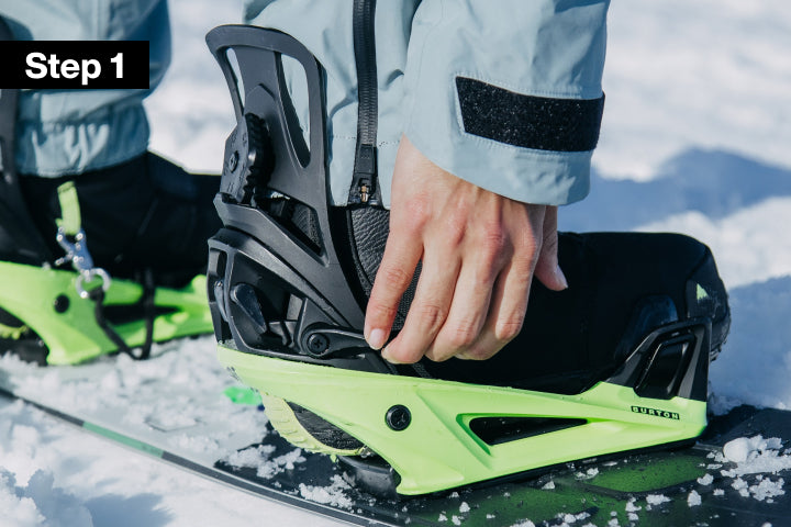 Person standing in a snowboard binding and using their hand to release he lever of the binding 