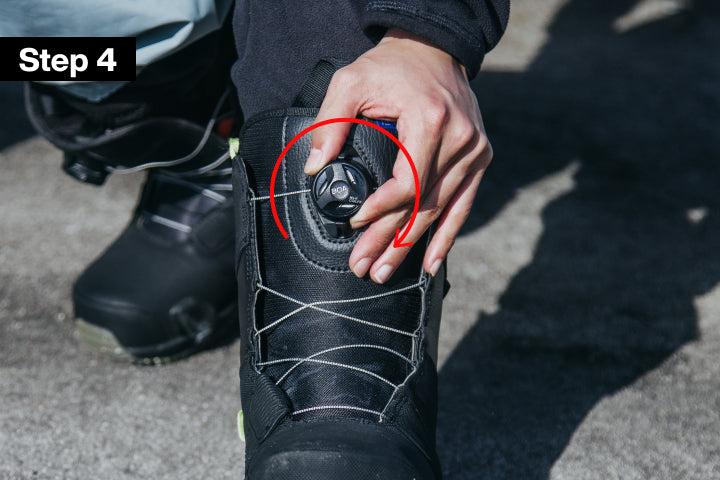 Close-up of a person's hand adjusting a black dial closure on a black snowboard boot, with a red circle highlighting the dial and a black overlay label reading 'Step 4'.