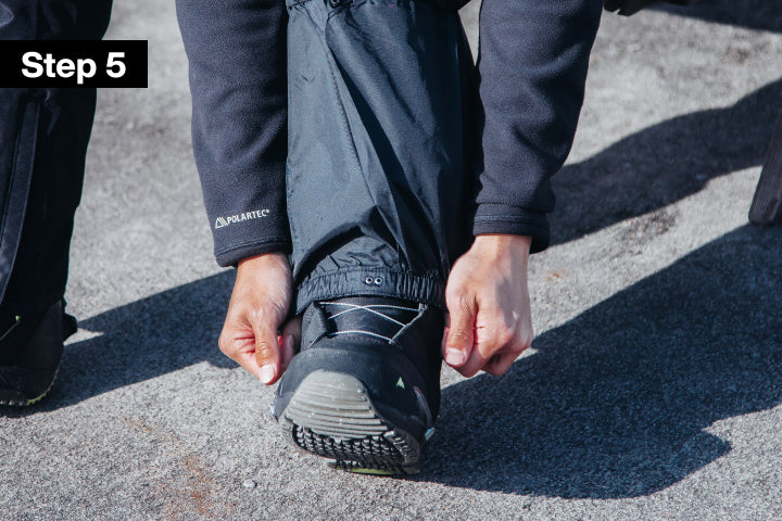 A close-up outdoor shot showing a person's hands adjusting the cuff of dark gray waterproof pants, pulling over a black boot. The image has a black overlay label in the top-left corner that reads 'Step 5'.
