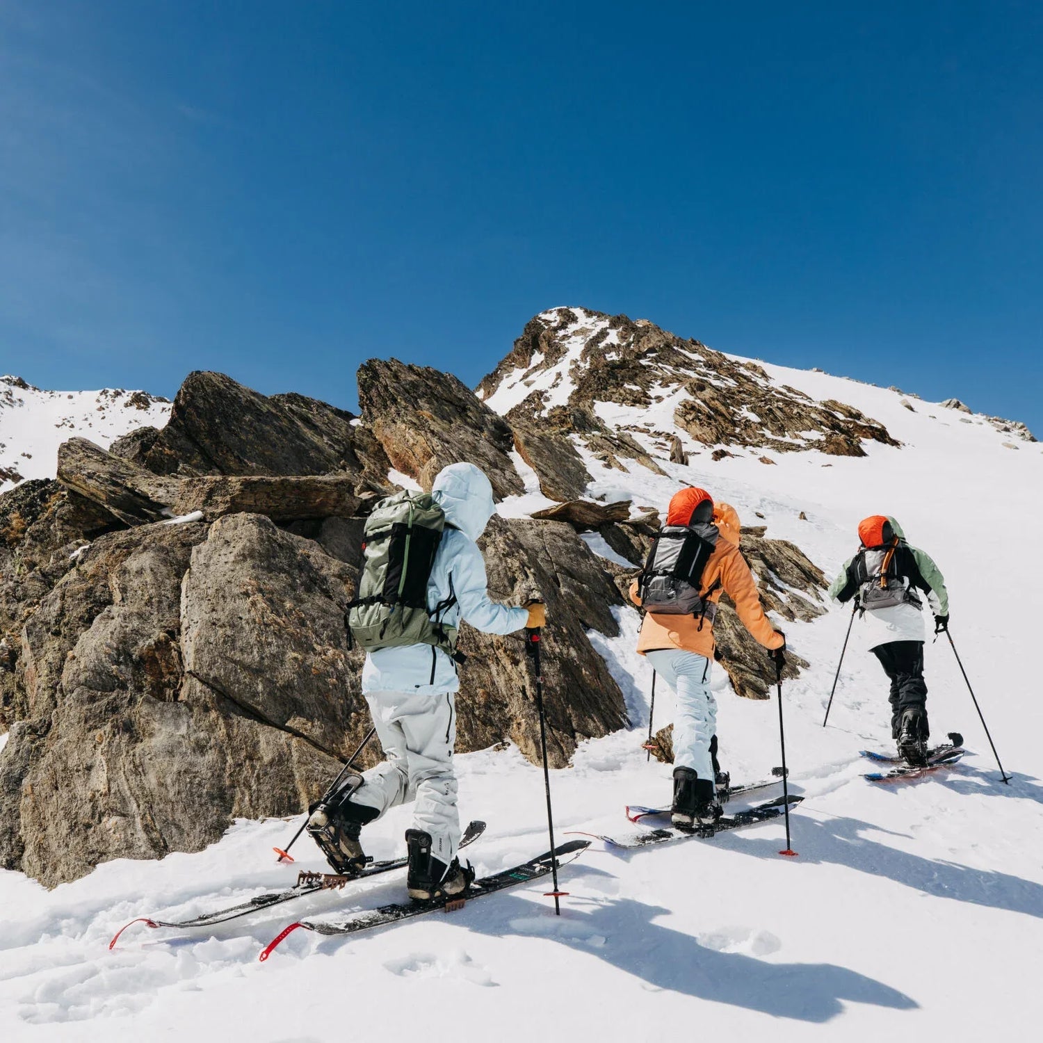 Three skiers on a snowy mountain with rocky outcrops and clear blue sky.